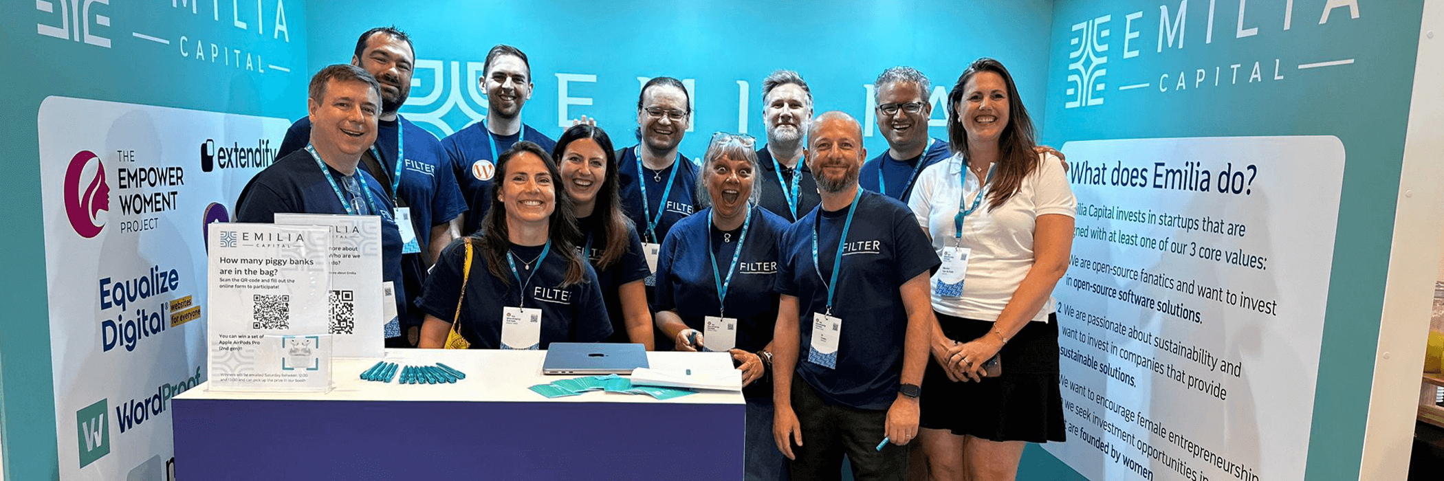 A group of people wearing matching blue shirts at a trade show booth with an Emilia Capital banner