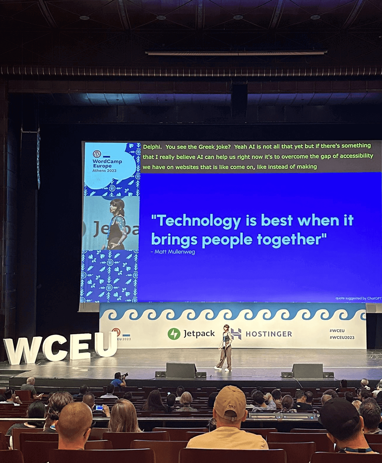 A speaker presents on stage at a conference with a large screen displaying the quote, "Technology is best when it brings people together." The auditorium is filled with attendees, and the stage is branded with "WCEU," Jetpack, and Hostinger logos.