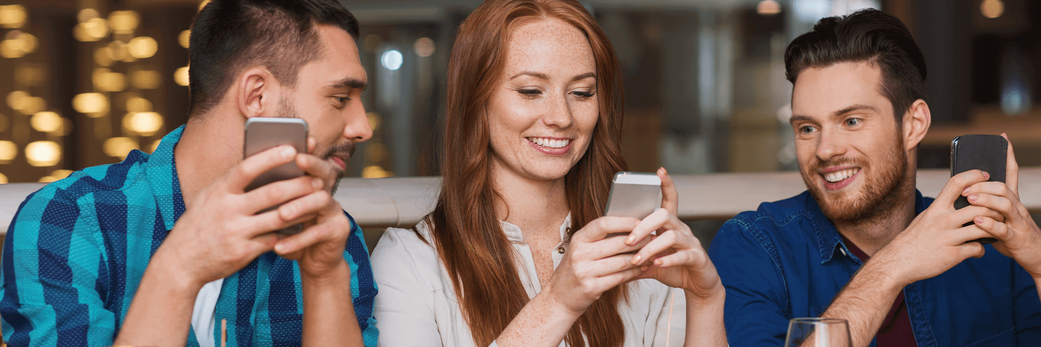 Three people sitting and engaging with smartphones in a casual setting, smiling and enjoying their time together.